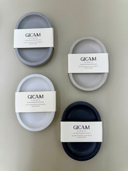 Four concrete soap dishes with GICAM Scents labels on a beige background