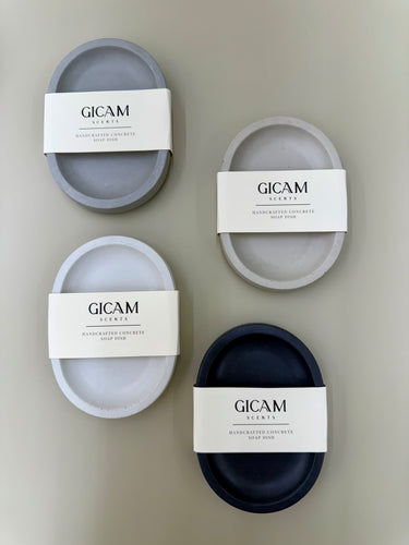 Four concrete soap dishes with GICAM Scents labels on a beige background