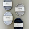 Four concrete soap dishes with GICAM Scents labels on a beige background